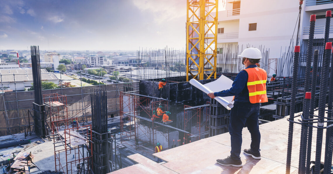 Construction workers build a multi-story structure with scaffolding, steel bars, and a crane. One worker holds blueprints.