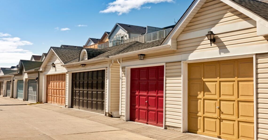 A row of garages with lanterns and different colored doors, including deep red, mustard yellow, and dark brown.
