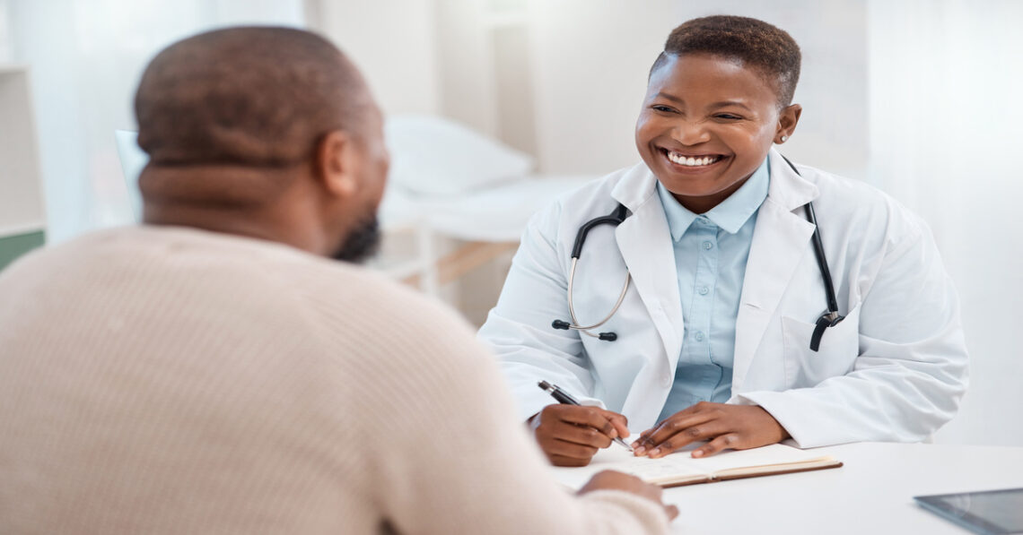 An urgent care doctor wearing a white coat and a stethoscope smiles at a patient. She is ready to write notes on a clipboard.