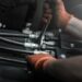 A close-up of someone wearing dirty orange work gloves while tightening an industrial hydraulic fitting.