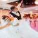 A bride and groom smile as he dips her on the dance floor. Confetti falls from the ceiling, and guests are in the background.