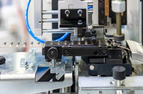 A side view of an automatic electric terminal crimping machine with a line of terminals feeding into the system.