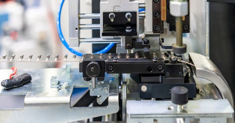 A side view of an automatic electric terminal crimping machine with a line of terminals feeding into the system.