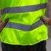 The view of someone from behind, with their hands on their hips, wearing a yellow high-visibility uniform during the day.