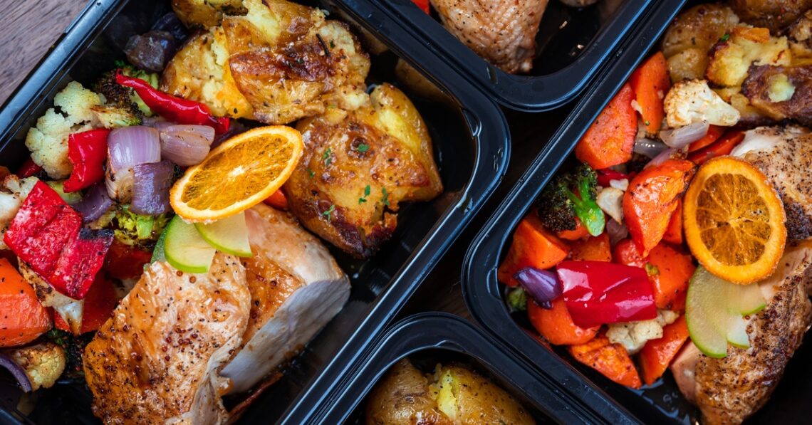 Meal prep containers sit on the counter with lean chicken and vegetables fully cooked and seasoned.