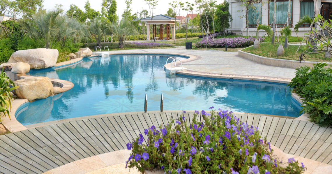 A luxury backyard pool with a rock feature and freshly groomed landscaping. The pool is curvy and bean-shaped.