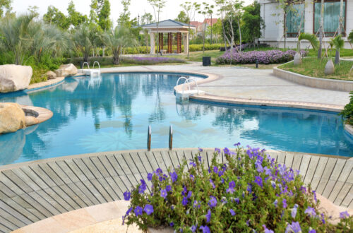 A luxury backyard pool with a rock feature and freshly groomed landscaping. The pool is curvy and bean-shaped.