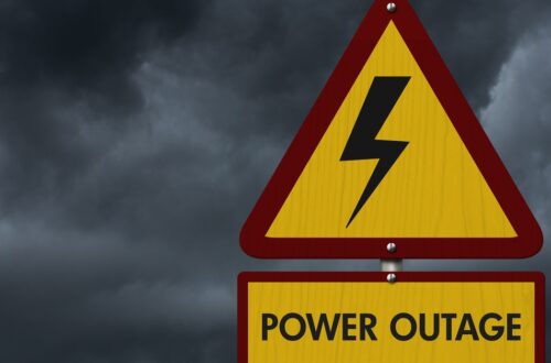 A yellow warning sign with a lightning bolt and “Power Outage” text against dark storm clouds in the background.