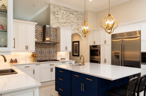 A large modern kitchen with white cabinets and a center island with navy cabinets. Backsplash and pendant lights decorate the space.