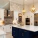 A large modern kitchen with white cabinets and a center island with navy cabinets. Backsplash and pendant lights decorate the space.