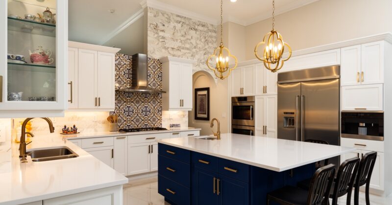A large modern kitchen with white cabinets and a center island with navy cabinets. Backsplash and pendant lights decorate the space.