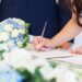 Bride signs a wedding license at a table, pen in hand, capturing a quiet, official moment after the ceremony.