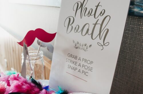 A photo booth setup with props beside a decorative sign reading “Photo Booth. Grab a prop, strike a pose, snap a pic”.
