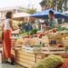 A woman stands at a farmers' market booth shopping for fresh produce. The booth is made out of wooden crates.