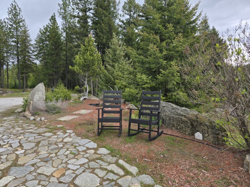 Outdoor seating area with 2 Greenvines rocking chairs on a stone patio, trees in the background.