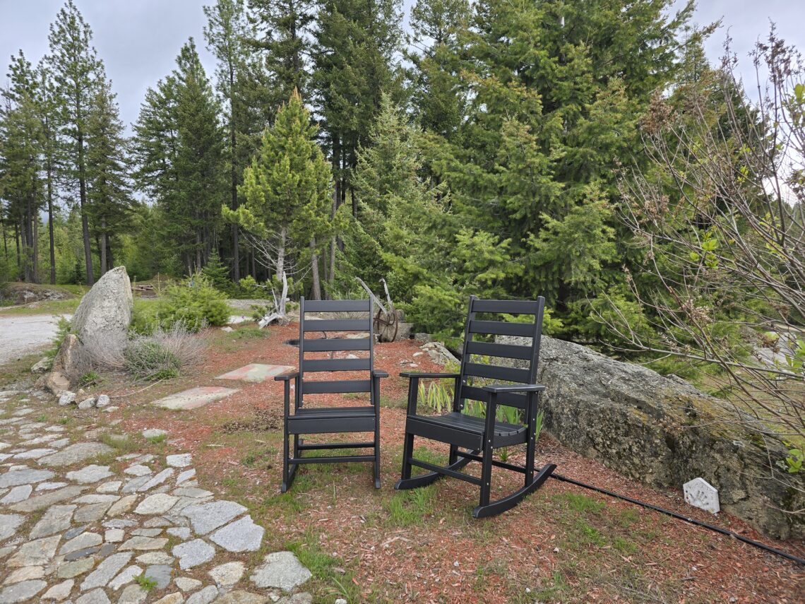 Outdoor seating area with 2 Greenvines rocking chairs on a stone patio, trees in the background.