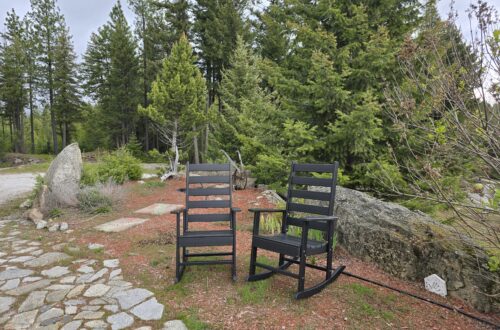 Outdoor seating area with 2 Greenvines rocking chairs on a stone patio, trees in the background.