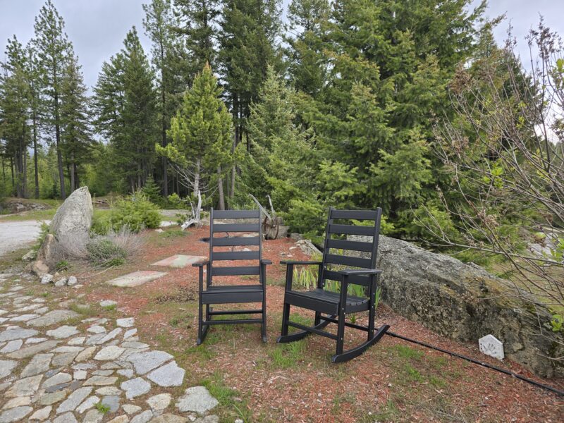Outdoor seating area with 2 Greenvines rocking chairs on a stone patio, trees in the background..