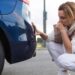 A woman looking at her back bumper after a minor accident. She is crouched behind the vehicle, her hand over her mouth.