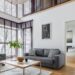 Modern living room with gray sofa and armchair, large windows with blinds, coffee table and rug in bright interior.