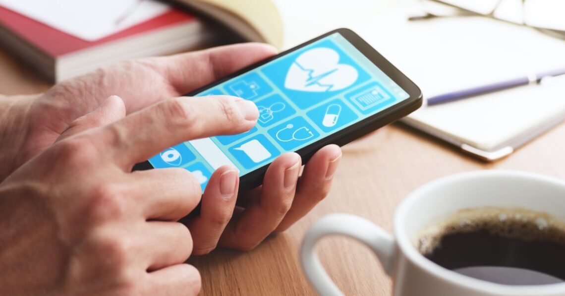 A pair of hands holding onto a smartphone with its screen on. The phone is next to a full cup of coffee.