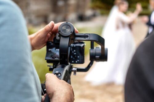 A person aiming a camera on a swivel mount toward a bride and groom. They're using both hands to hold the camera steady.