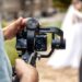 A person aiming a camera on a swivel mount toward a bride and groom. They're using both hands to hold the camera steady.