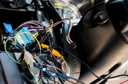 A car interior during the daytime. A panel is popped out of the dashboard to reveal colorful wires sticking out.