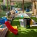 A covered backyard patio contains toys, a couch, and scattered clutter as the family space spills into the yard.
