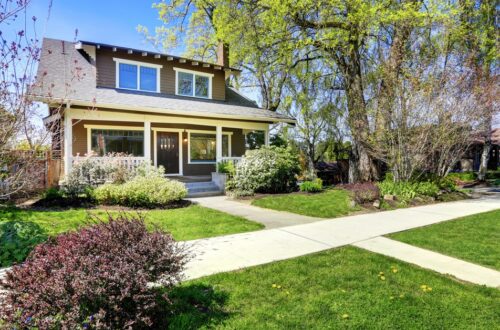 A view of a nice two-story home from a sidewalk with green grass growing in the yard and a blue sky background.