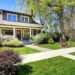 A view of a nice two-story home from a sidewalk with green grass growing in the yard and a blue sky background.