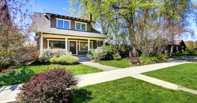 A view of a nice two-story home from a sidewalk with green grass growing in the yard and a blue sky background.