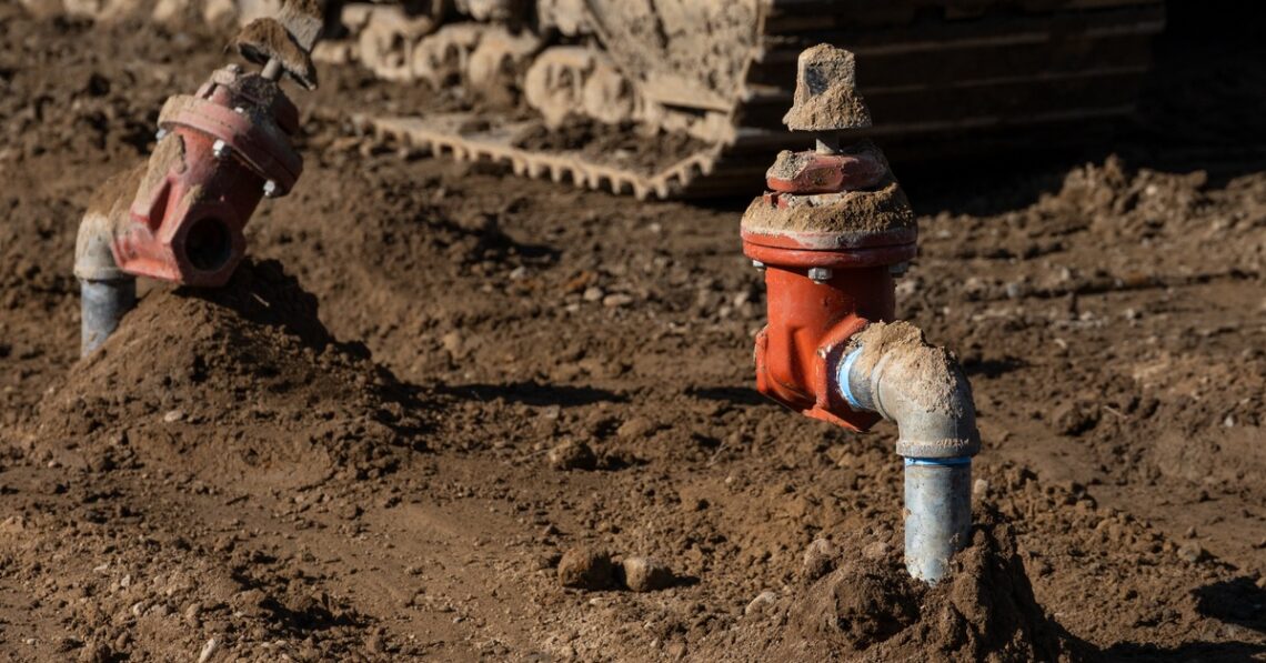 A dirt covered area with two pipe spickets coming out of the ground. The spickets have water shutoff valves.