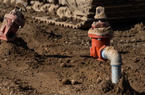 A dirt covered area with two pipe spickets coming out of the ground. The spickets have water shutoff valves.