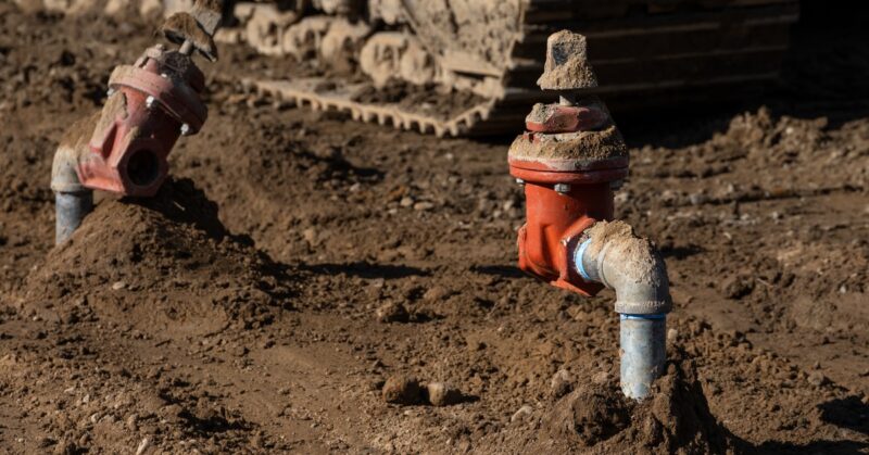 A dirt covered area with two pipe spickets coming out of the ground. The spickets have water shutoff valves.