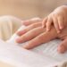 A close-up of a parent's hand on their Bible with their small child's hand on the adults. They're reading together.