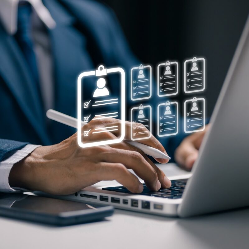 A recruiter working on a laptop. Small profile icons representing job candidates are displayed above the laptop.