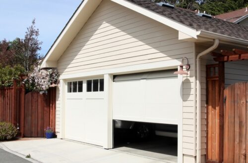 A sunny day in an alleyway with a two car garage. One garage door is shut and the other is half open.