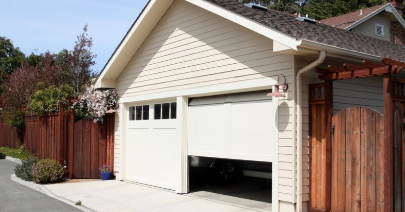 A sunny day in an alleyway with a two car garage. One garage door is shut and the other is half open.