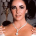 Elegant Elizabeth Taylor wearing a diamond necklace and earrings, with hands resting on her shoulders in a formal pose.