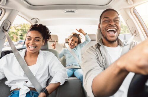 A family of three enjoying a car ride. The parents are in the front seat, and the daughter is in the back seat singing.