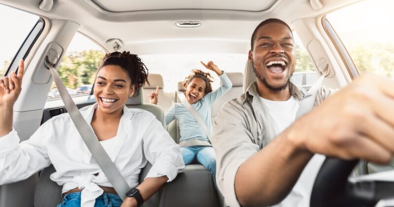 A family of three enjoying a car ride. The parents are in the front seat, and the daughter is in the back seat singing.