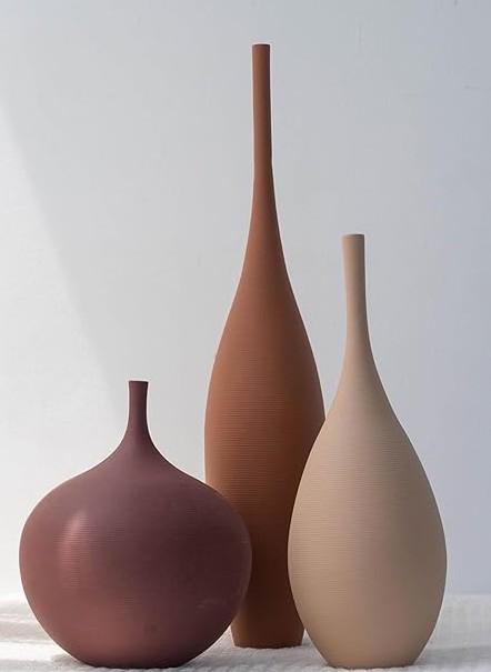 Three matte ceramic vases in burgundy, terracotta, and beige sit on a light surface.