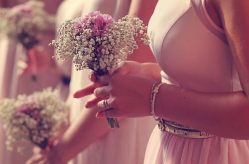 A woman in a pink dress holding a white baby’s breath bouquet tied with a pink ribbon in bright sunlight.