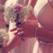A woman in a pink dress holding a white baby’s breath bouquet tied with a pink ribbon in bright sunlight.