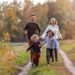 A young family of four running together between dirt tracks on the grass. The two children are holding hands.