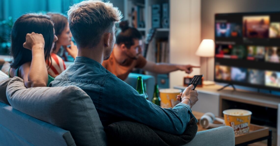 People on a sofa watching TV together, one holds a remote while a streaming service fills the screen.