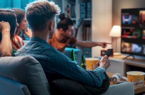 People on a sofa watching TV together, one holds a remote while a streaming service fills the screen.