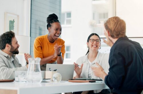 A marketing team of four professionals sits happily around a conference table to discuss brand awareness.
