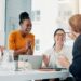 A marketing team of four professionals sits happily around a conference table to discuss brand awareness.